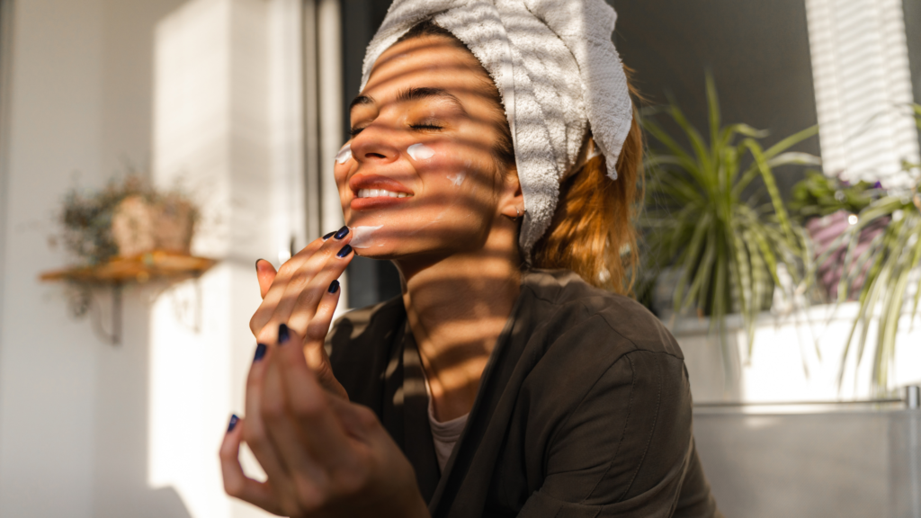 Beautiful young woman wearing a towel on her head putting on face lotion as she learns to self love